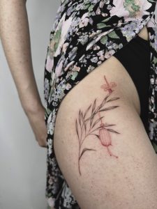 delikatny, graficzny tatuaż na udzie motyw rośliny