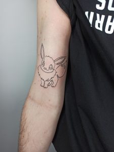 Tatuaż na bicepsie przedstawiający królika w prostym konturze, modny tatuaż zwierzęcy na 2024 rok
