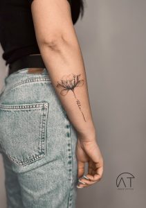 Minimalistyczny tatuaż kwiatowy na boku przedramienia, pokazujący pojedynczą gałązkę z kwiatami, trend tatuaże kwiaty 2024