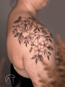 Tatuaż przedstawiający dużą kompozycję kwiatową na ramieniu, z różami i liśćmi w odcieniach szarości, modne tatuaże kwiaty 2024
