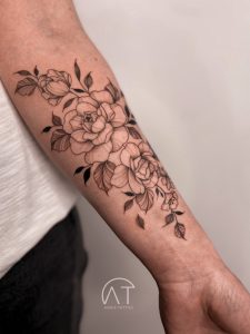 Modny w 2024 roku tatuaż z delikatnymi kwiatami na przedramieniu, przedstawiający rozkwitłe peonie w stylu graficznym