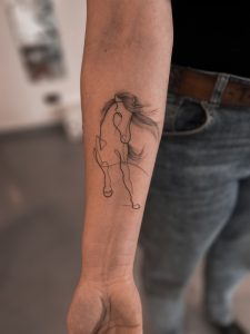 Tatuaż na ramieniu z konturem abstrakcyjnego konia, modne tatuaże zwierzęce na 2024 rok
