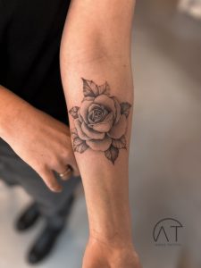 Tatuaż na przedramieniu z elegancką różą w towarzystwie małych kwiatów, wyrafinowany styl kwiatowych tatuaży na 2024 rok.