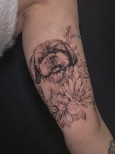 Szczegółowy tatuaż na ramieniu przedstawiający głowę psa otoczoną przez kwiaty, wskazujący na modę tatuaży zwierzęcych na 2024 rok.