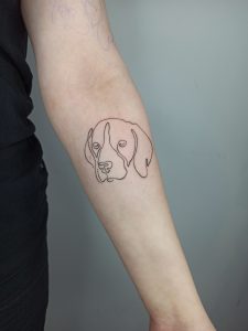 Tatuaż na ramieniu z minimalistycznym konturem psa, trendy tatuaże zwierzęta 2024