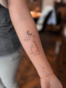 Minimalistyczny tatuaż kota z księżycem – subtelny wzór na przedramieniu