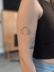 Minimalistyczny tatuaż psa – delikatny kontur pupila na ramieniu