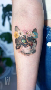 Tatuaż pieska, kota, pupila - przykładowe wzory i inspiracje 21 Kolorowy tatuaż kota z kwiatami – realistyczny portret pupila na przedramieniu