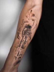 Tatuaż konceptualny z astronautą na przedramieniu Tatuaż konceptualny z astronautą, planetami i geometrycznymi detalami na przedramieniu